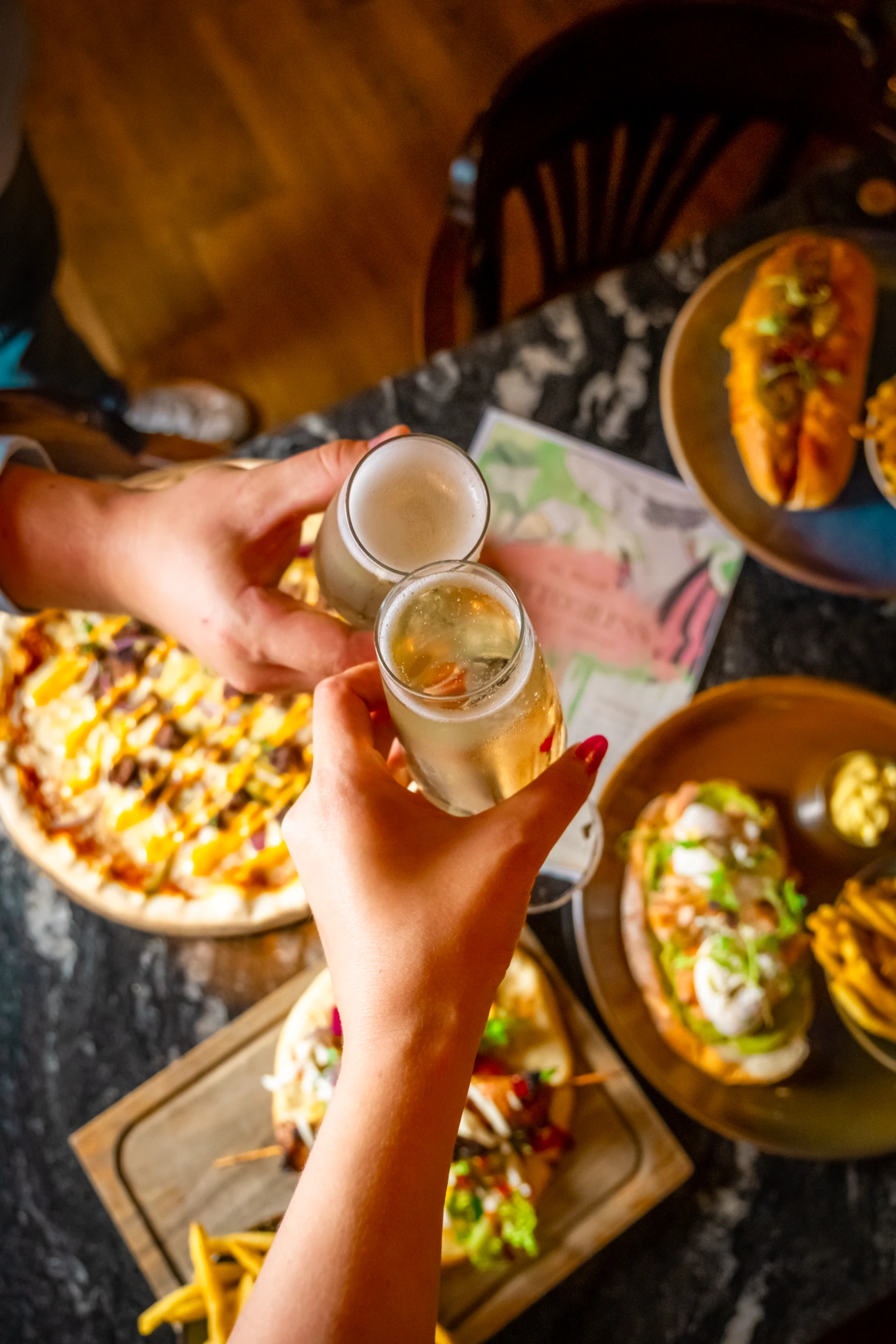 Two guests toasting drinks over a table of Al Bear food
